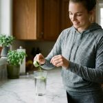 Jeune femme sportive versant poudre verte dans un verre d'eau