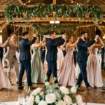 Invités de mariage dansant le Madison en groupe dans une grange décorée de guirlandes et de verdure